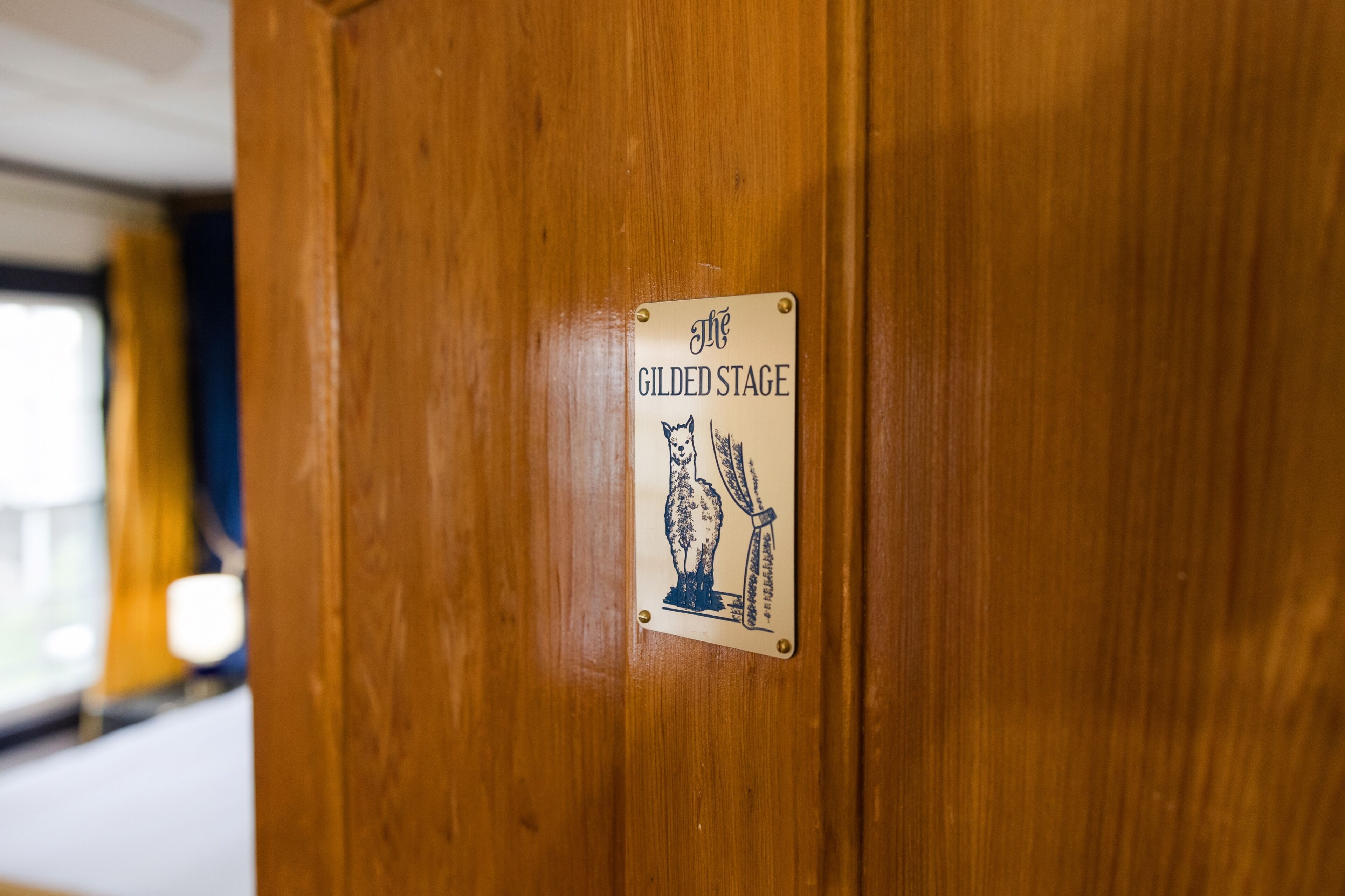 Eine Holztür mit einem Schild, auf dem 'The Gilded Stage' steht.