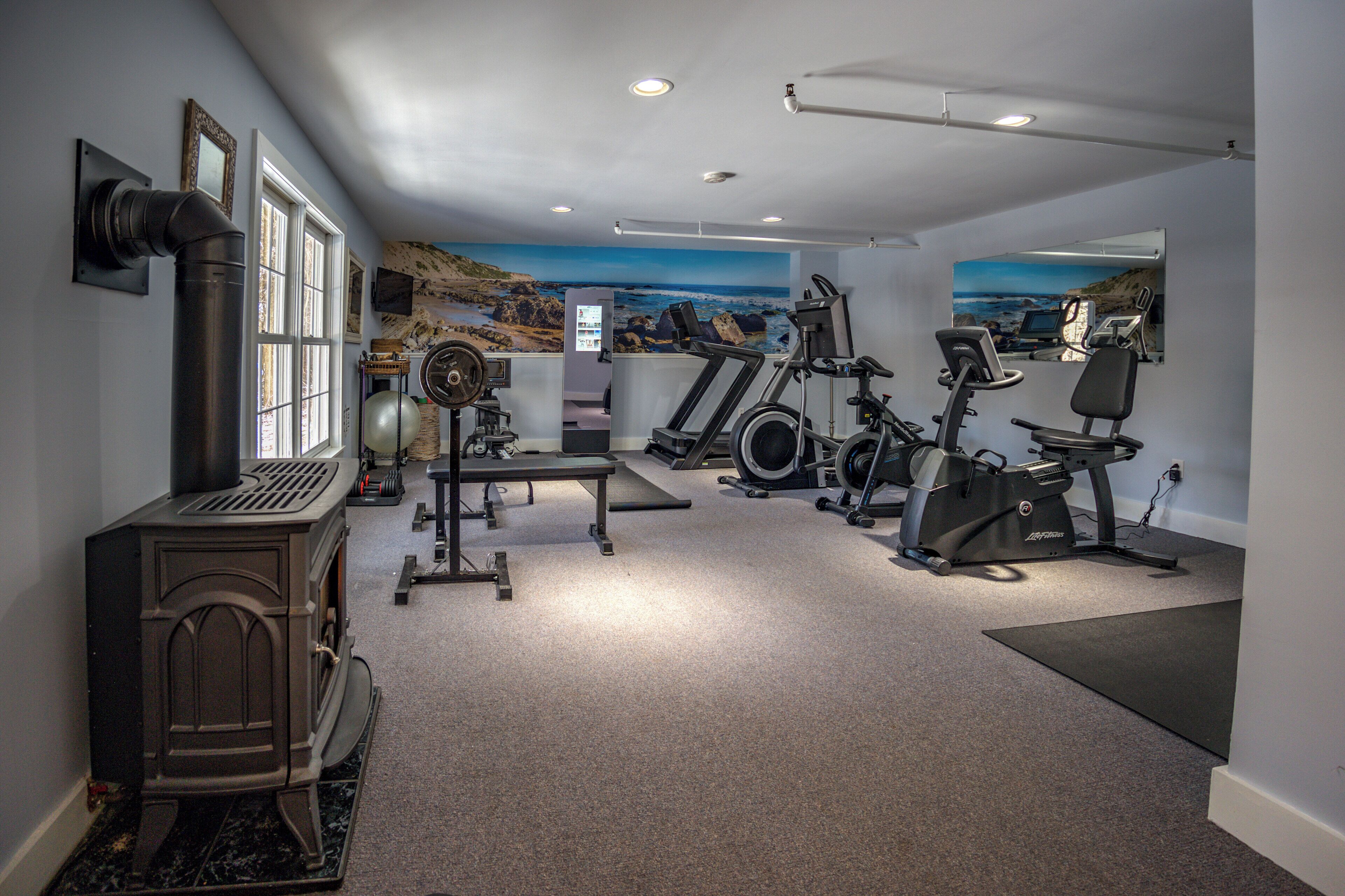 A home gym with exercise equipment, a fireplace, and scenic wall art.