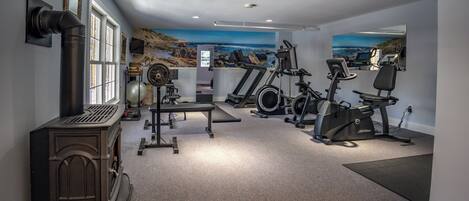 A home gym with exercise equipment, a fireplace, and scenic wall art.