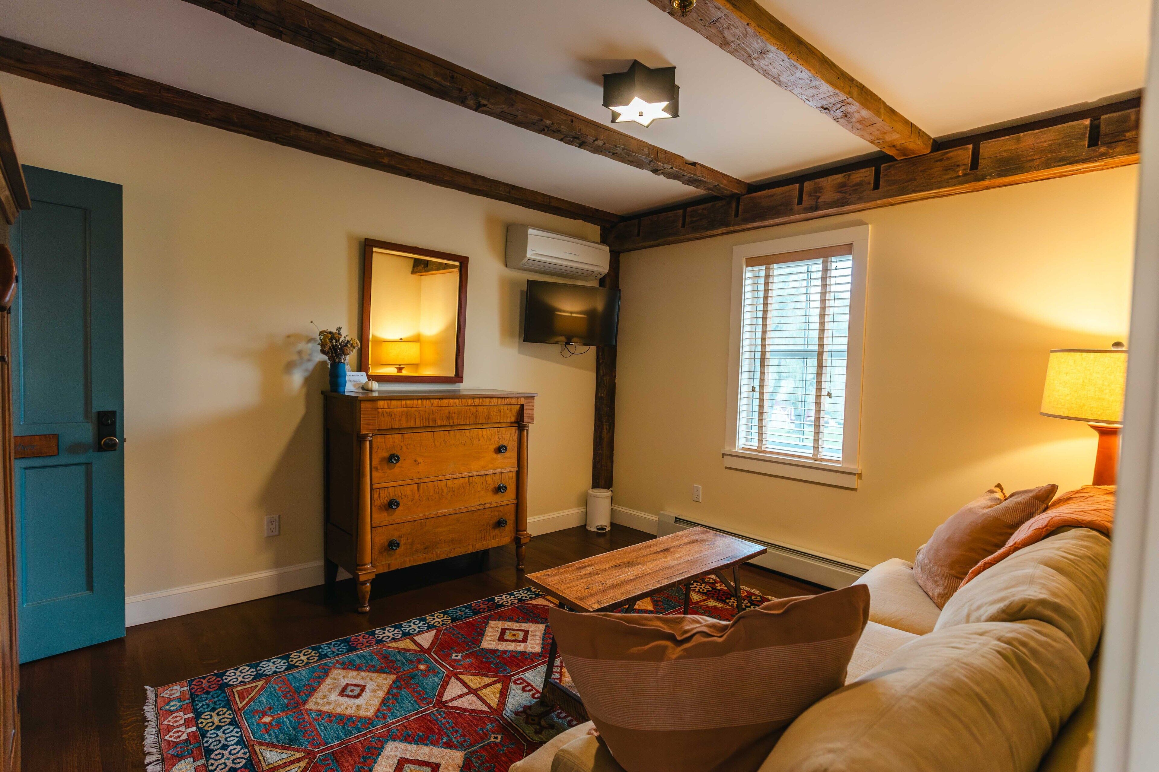 A cozy room with a wooden dresser, a bench, a bed with pillows, a patterned rug, a star-shaped ceiling light, and a window with blinds.