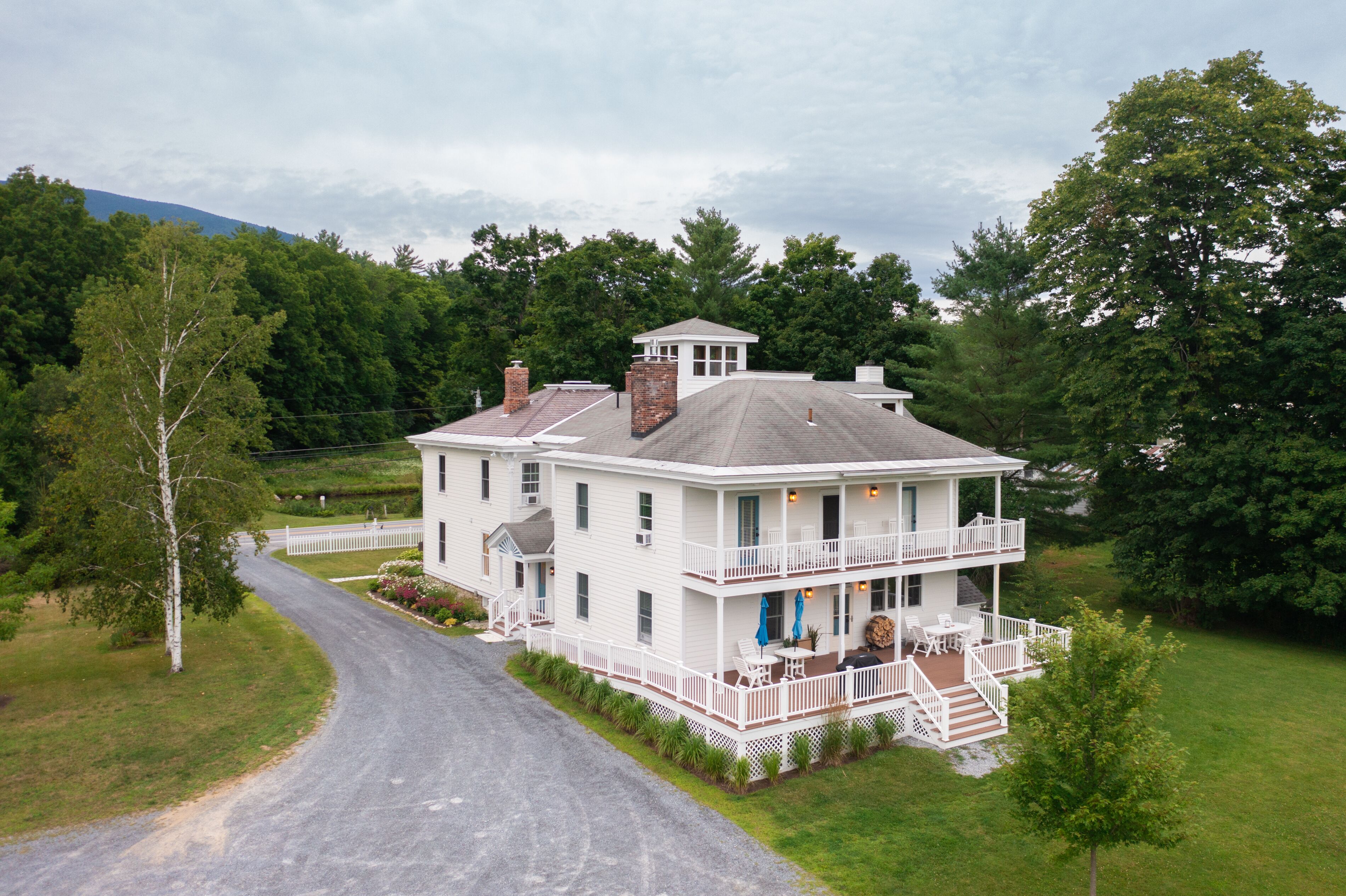 A two-story white house with a balcony, surrounded by greenery and a driveway.