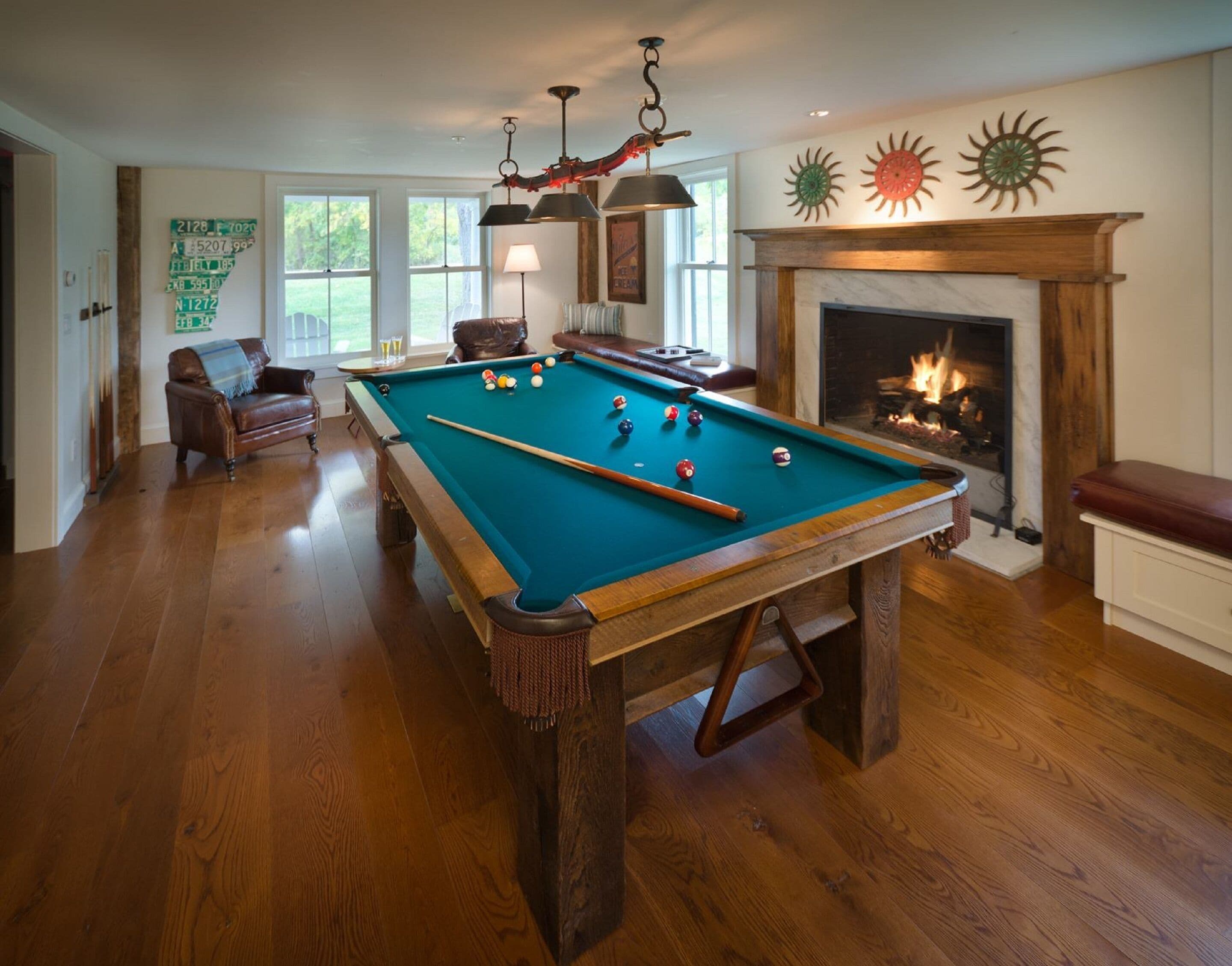 A pool table in a room with hardwood floors, a fireplace, and a view of the outdoors.