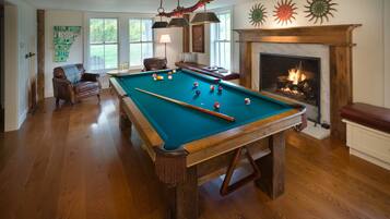 A pool table in a room with hardwood floors, a fireplace, and a view of the outdoors.