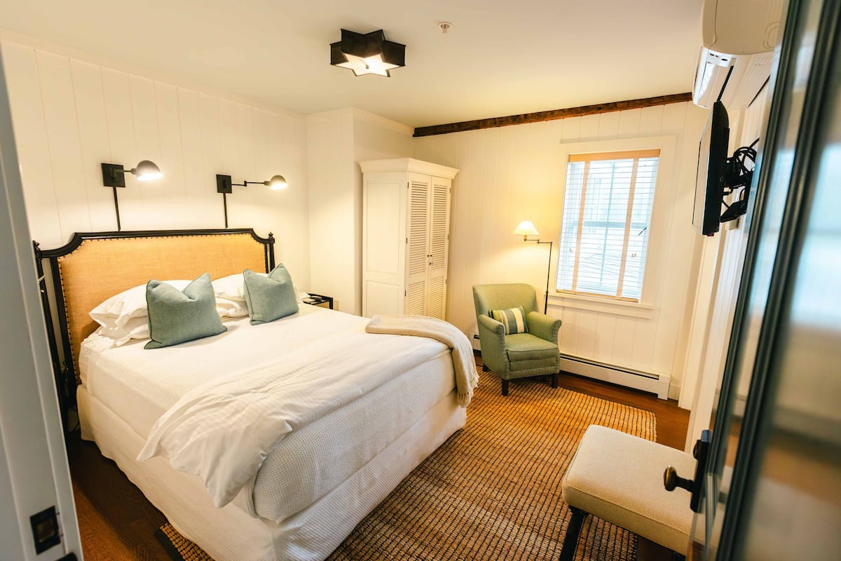 A hotel room with a large bed, a chair, a wardrobe, and a window.