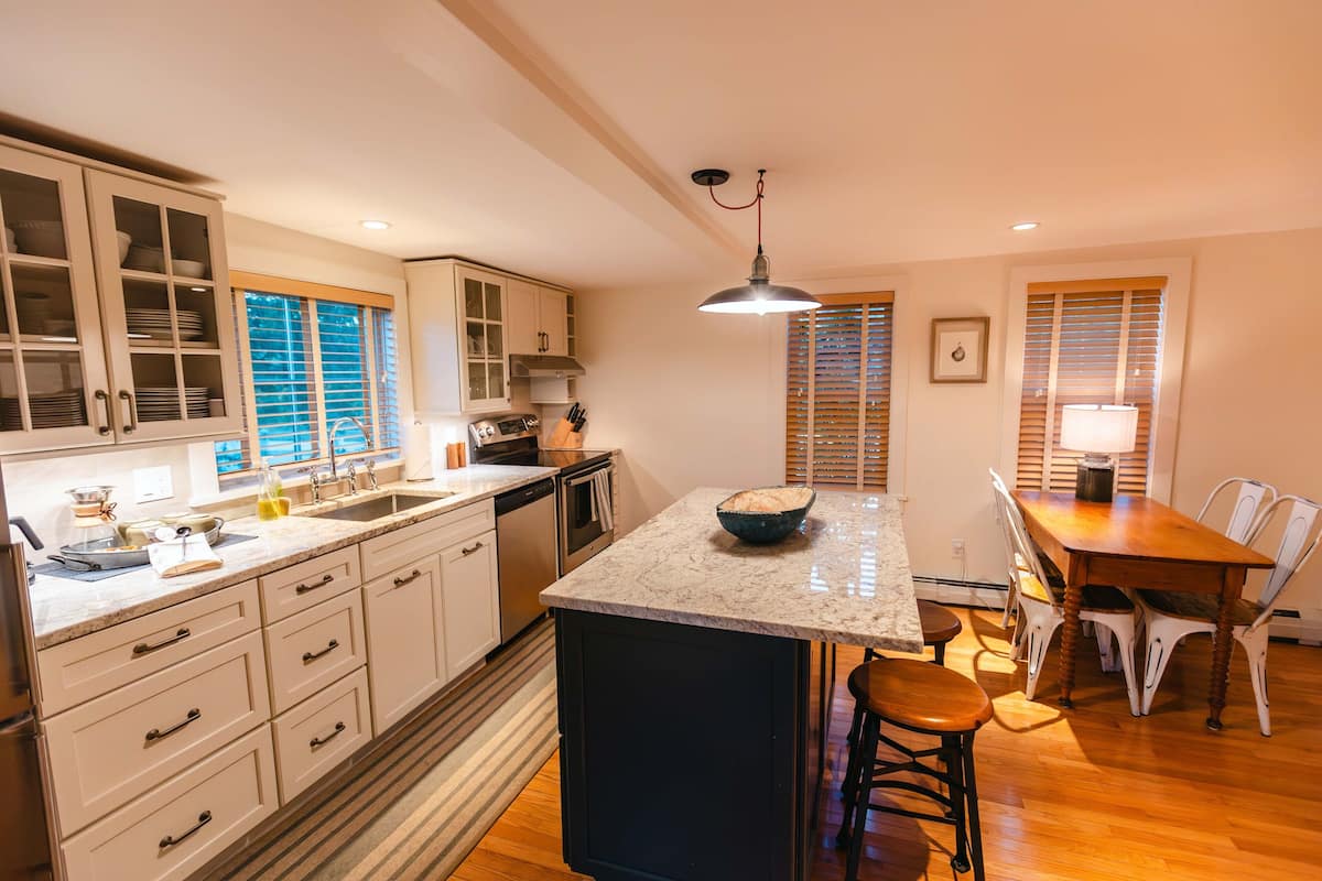 A kitchen with a central island, wooden dining table, and white cabinetry.