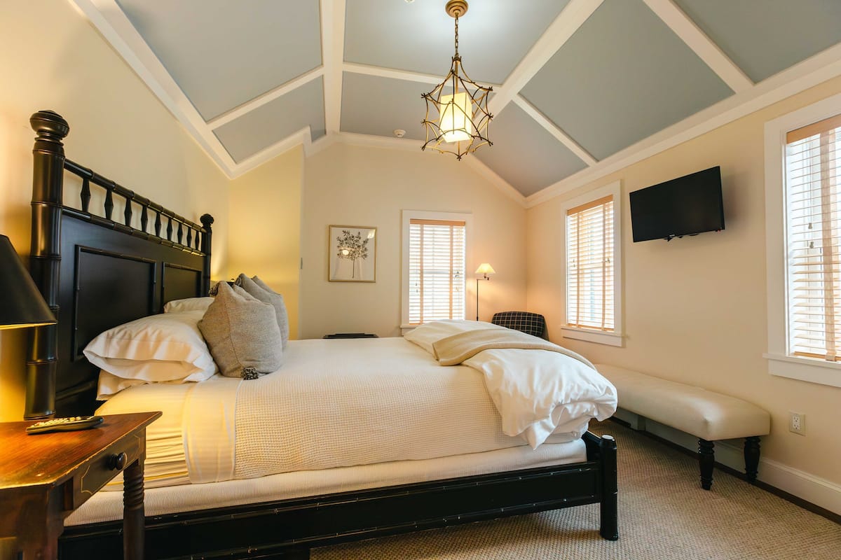 A bedroom with a bed, bedside lamp, bench, and a ceiling light fixture.