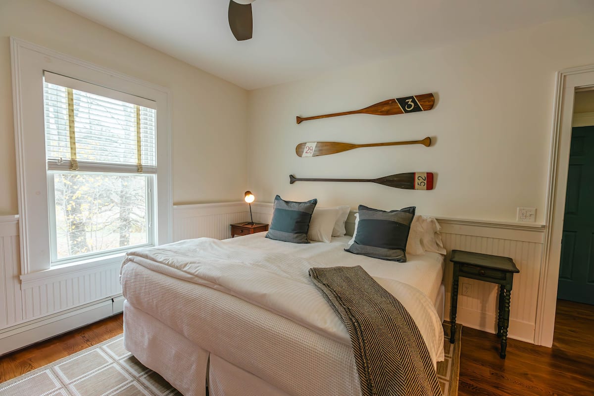 A bedroom with a large bed, a nightstand with a lamp, and two wall-mounted paddles.