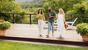 A wooden deck with potted plants, a white chair, and a scenic view of hills and trees. - Hill Farm Inn (Arlington)