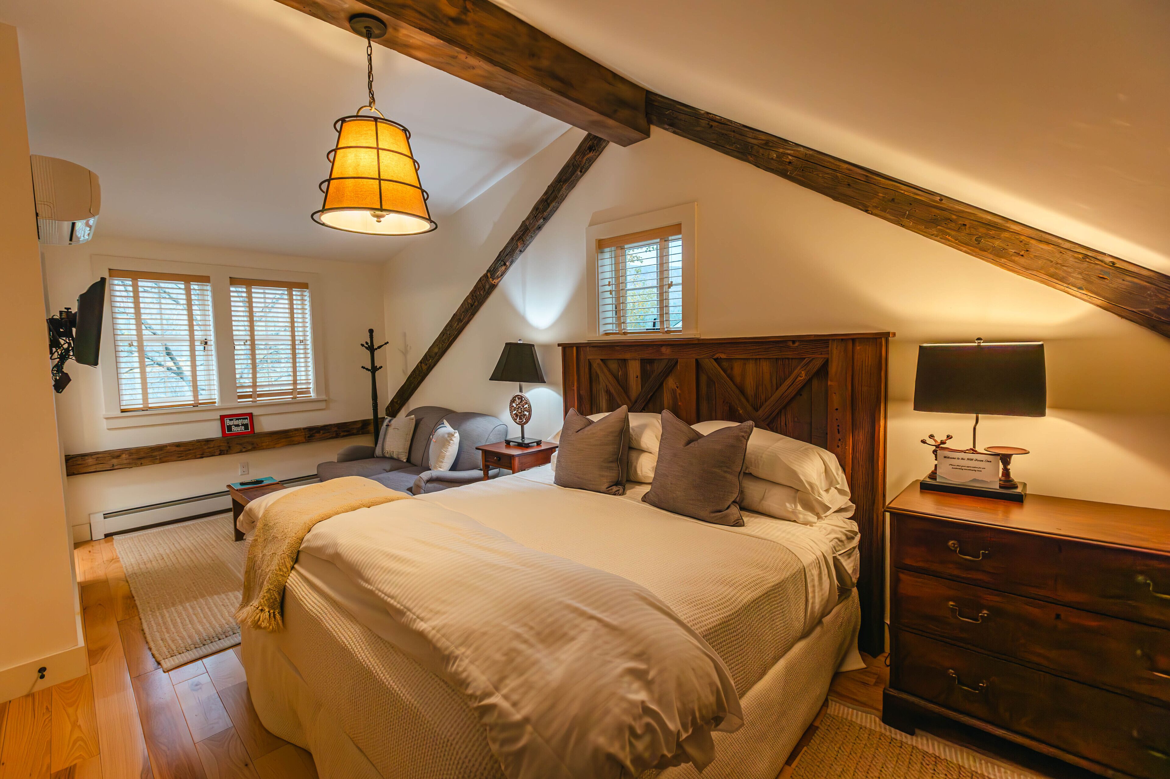 A bedroom with a large bed, wooden headboard, two bedside tables with lamps, a dresser, and a window with blinds.