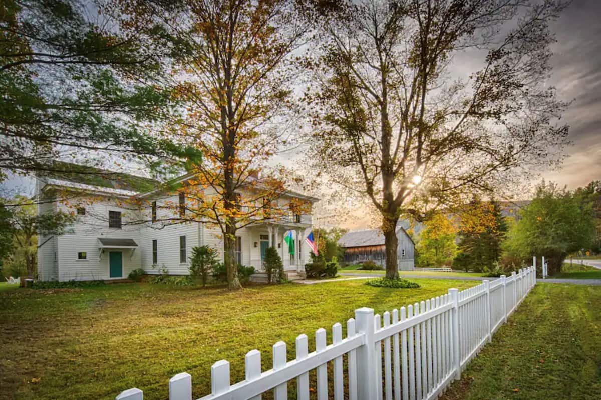 A white house with a front porch, surrounded by a white picket fence, and a grassy yard.