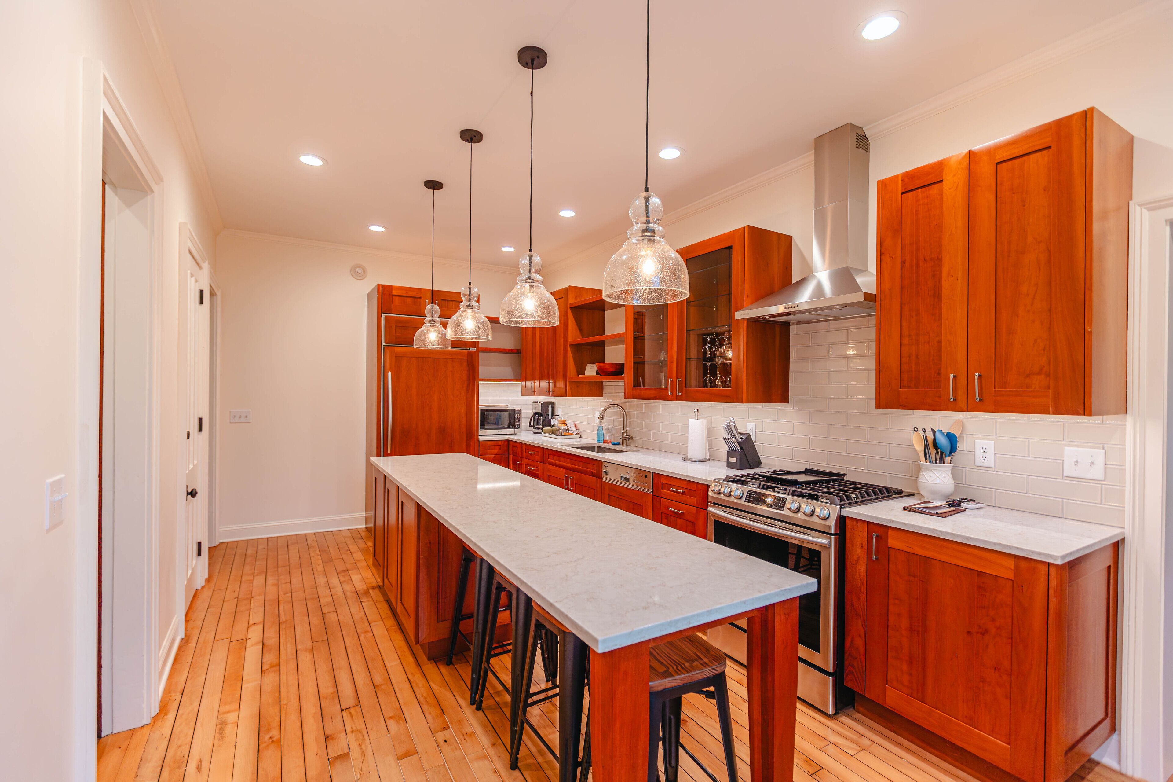 A modern kitchen with wooden cabinets, a large island, stainless steel appliances, and pendant lighting.
