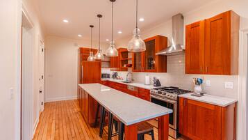 A modern kitchen with wooden cabinets, a large island, stainless steel appliances, and pendant lighting.