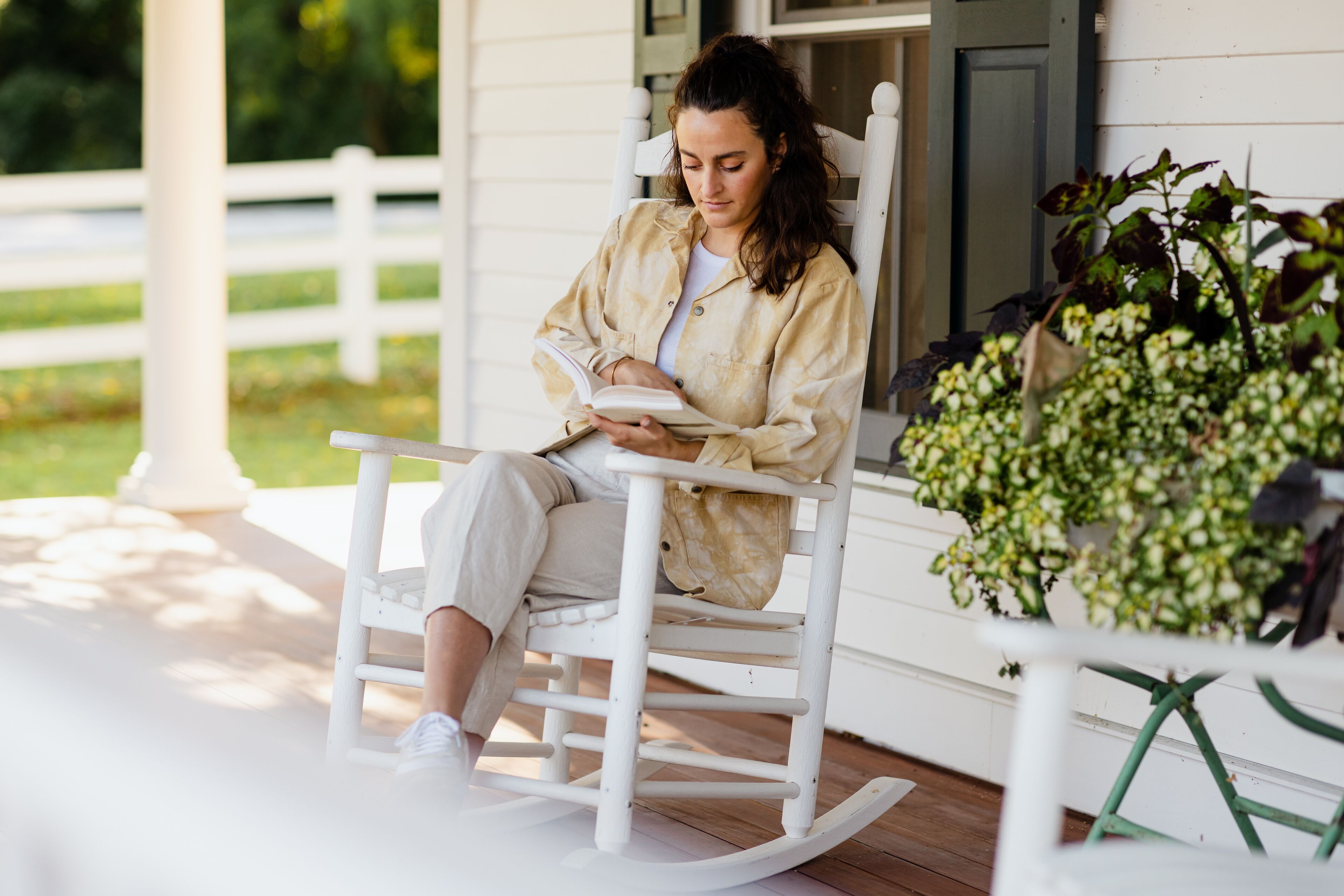 A person sitting on a rocking chair on a porch with a book.
