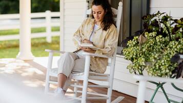 A person sitting on a rocking chair on a porch with a book.
