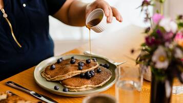 A breakfast setting with pancakes and blueberries on a plate, a cup of coffee, and a vase of flowers.