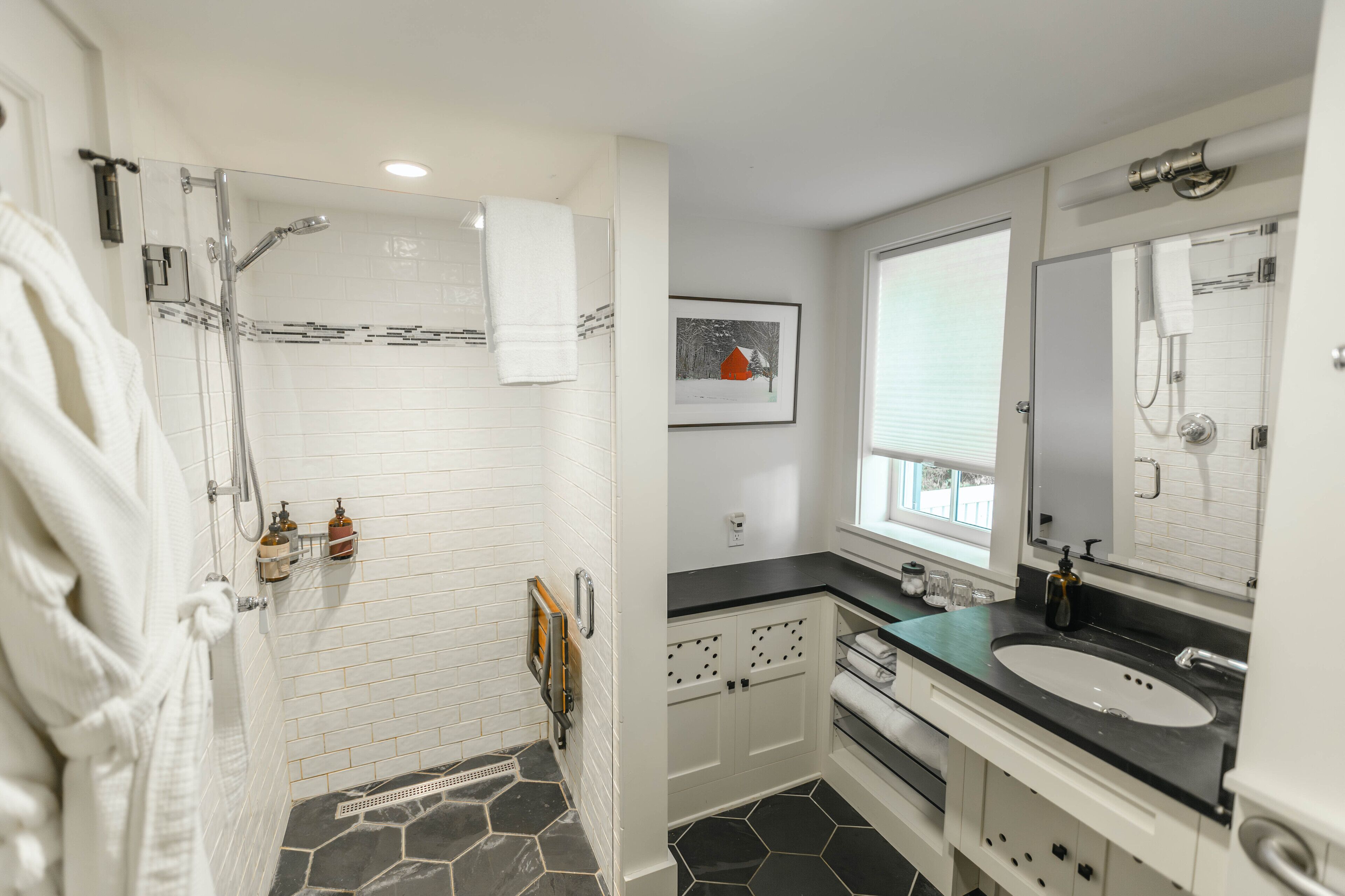 A modern bathroom with a glass-enclosed shower, white tiled walls, a black countertop sink, and a large mirror.