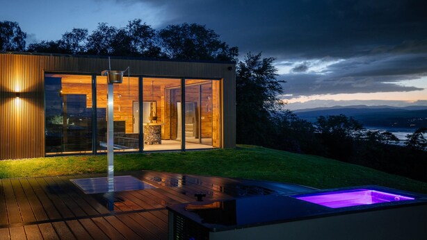 A modern house with large glass windows, a wooden deck, and a hot tub.