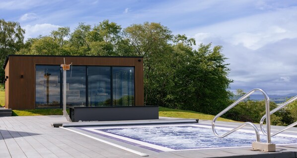 A modern outdoor hot tub area with a wooden deck, a glass-enclosed structure, and a view of the surrounding greenery. - Gleddoch Golf & Spa Resort, WorldHotels Distinctive (Port Glasgow)