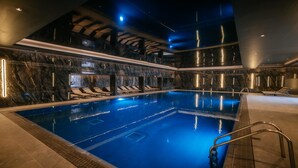 A large indoor swimming pool with marble walls and ceiling, surrounded by lounge chairs and a poolside area.