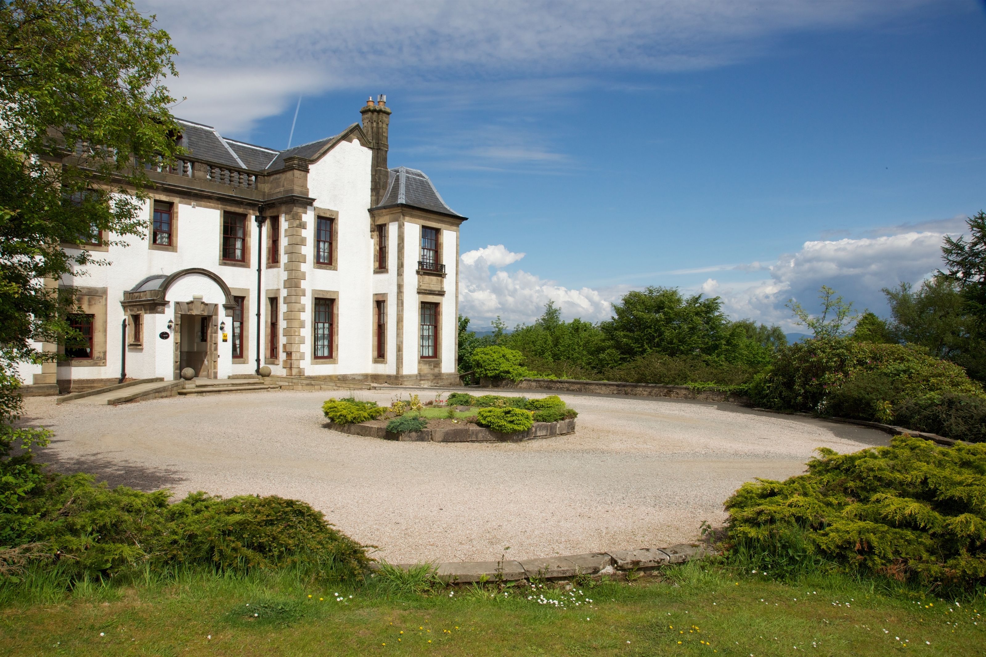 A large, white building with a symmetrical facade, a central entrance, and a gravel driveway leading to a circular driveway.