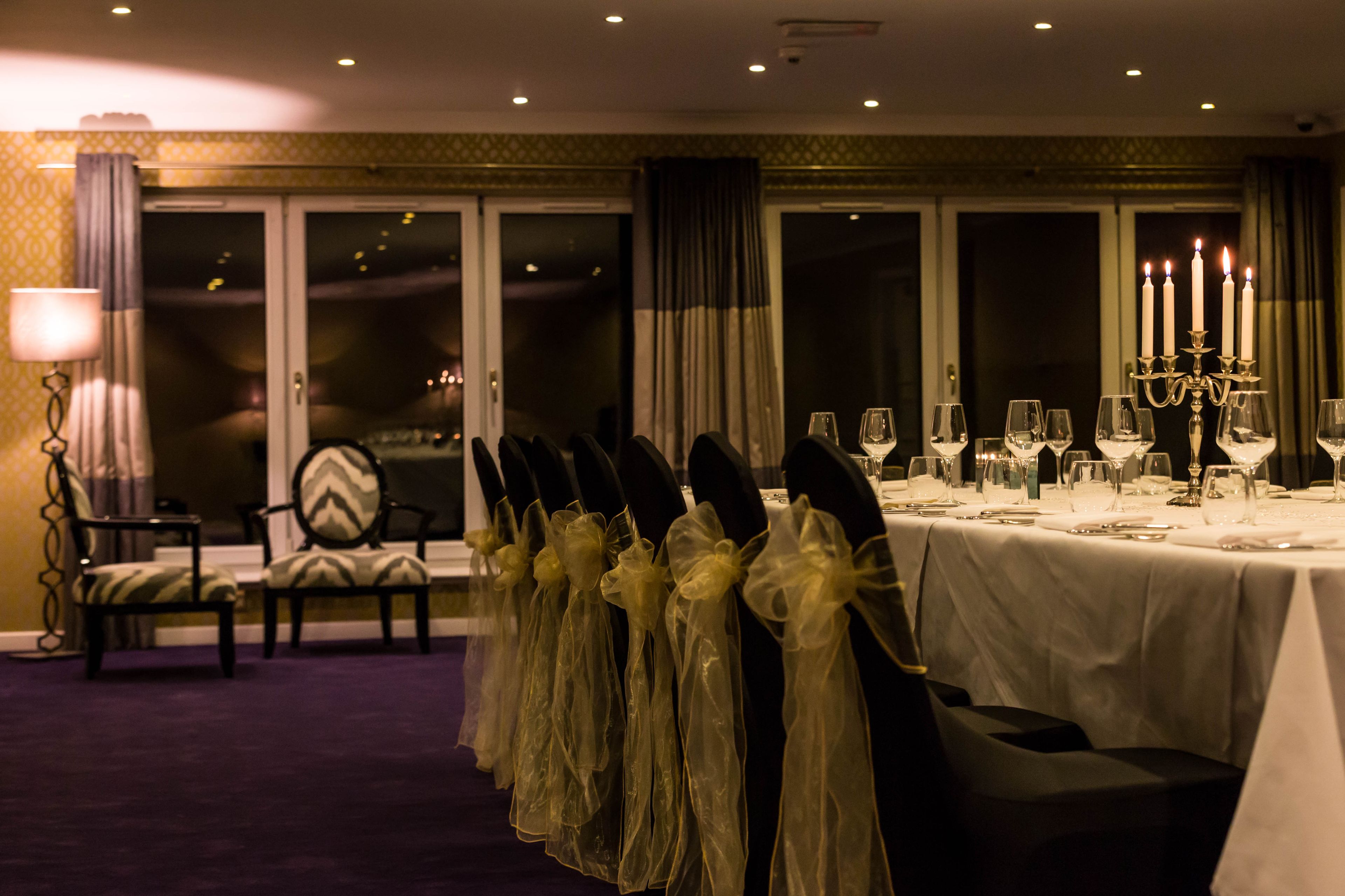 A dining area with a table set for a meal, chairs with ties, and a candelabra with candles.