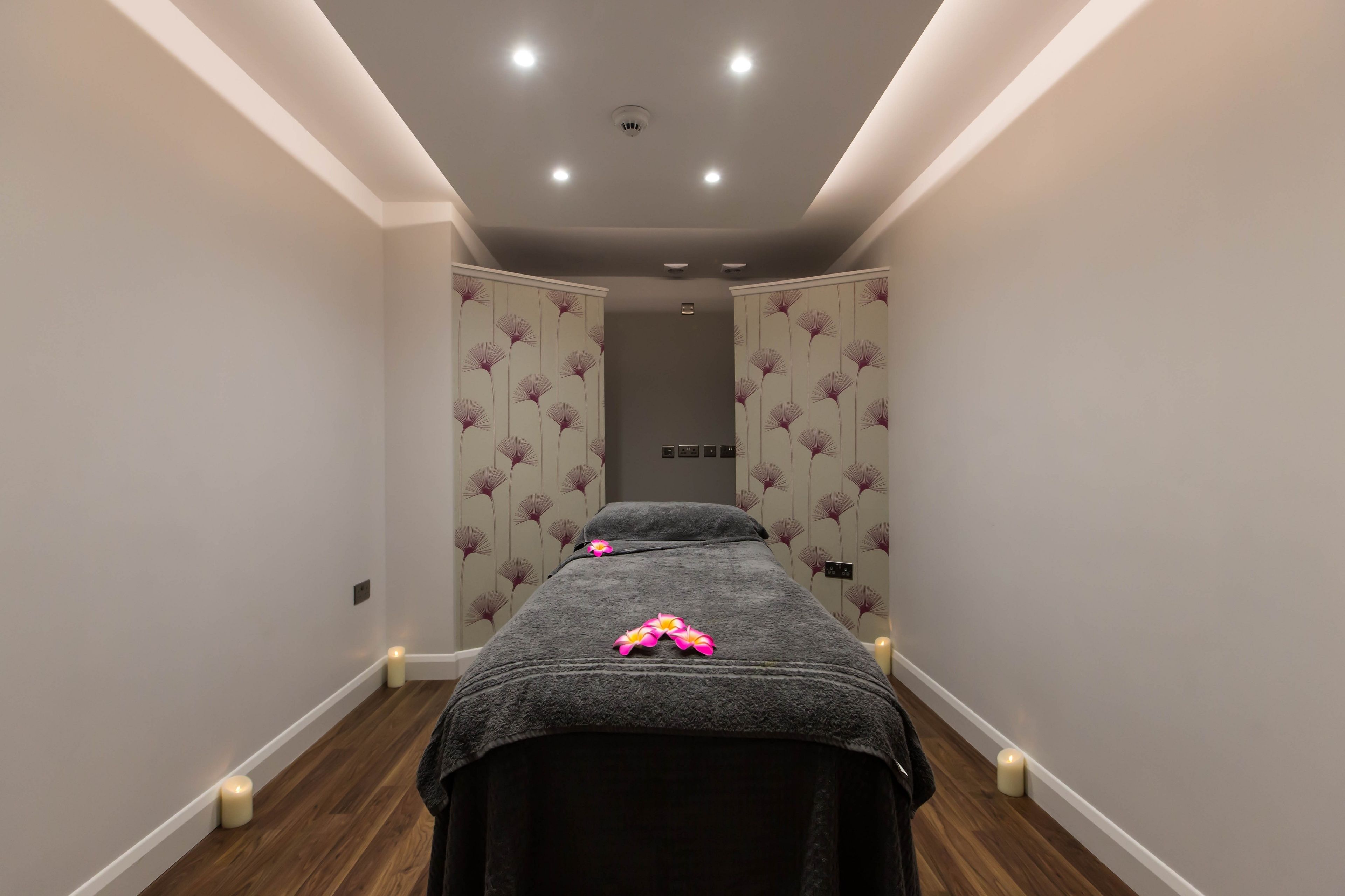 Un cuarto de spa con una camilla de masaje, velas y una lámpara en el techo.