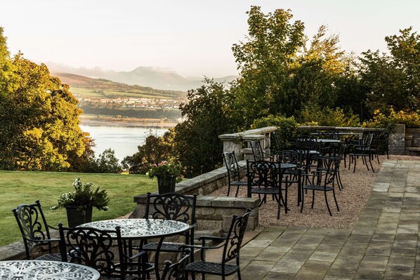 An outdoor patio with tables and chairs, overlooking a body of water and a distant town. - Gleddoch Golf & Spa Resort, WorldHotels Distinctive (Port Glasgow)