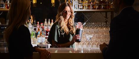 A bar area with a bartender preparing a drink, shelves with various bottles, and a bar counter.