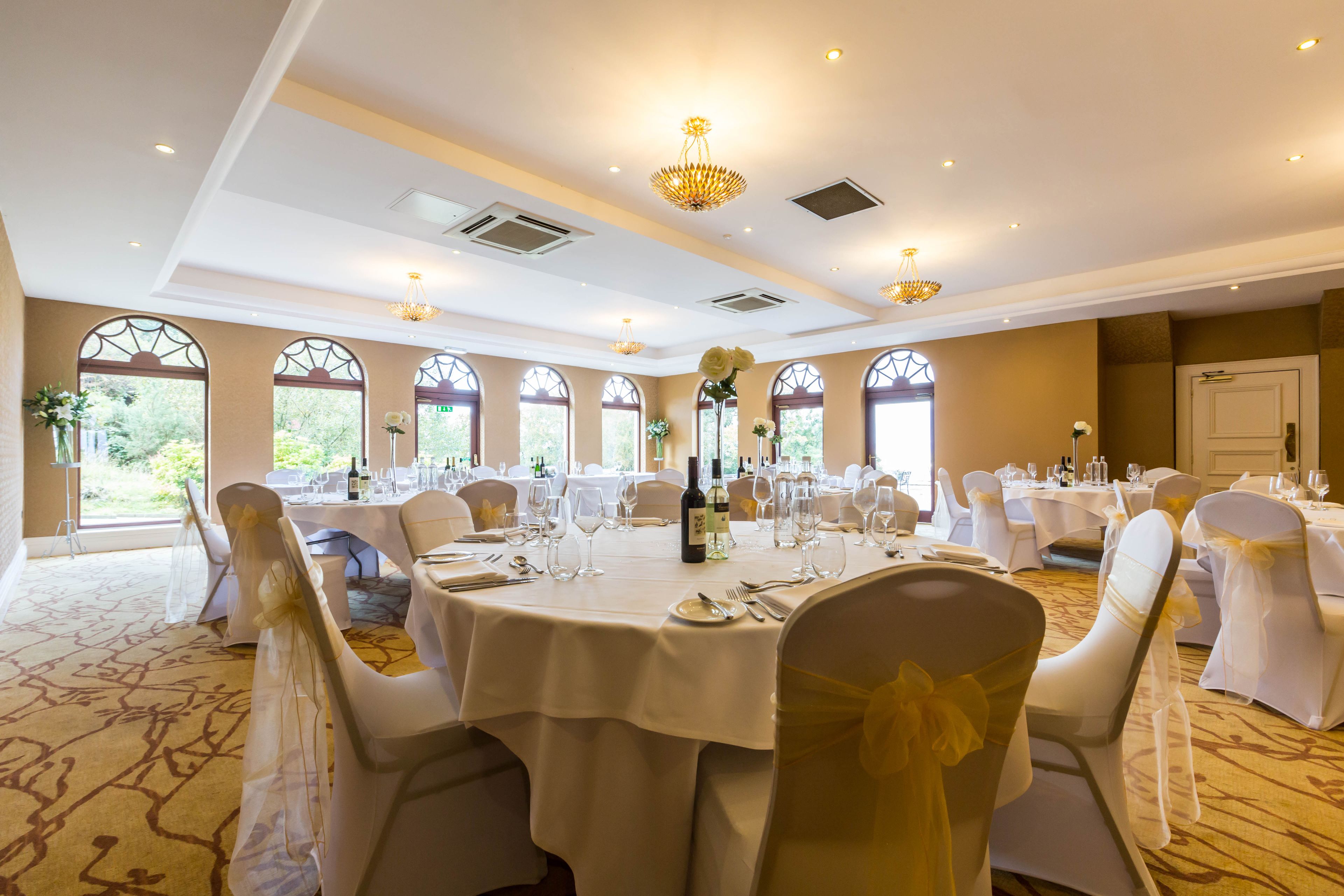 Une salle de banquet avec des tables rondes, des chaises blanches et des lustres.
