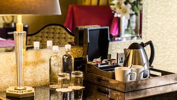 A hotel room's minibar with a lamp, bottles, glasses, and a coffee pot.