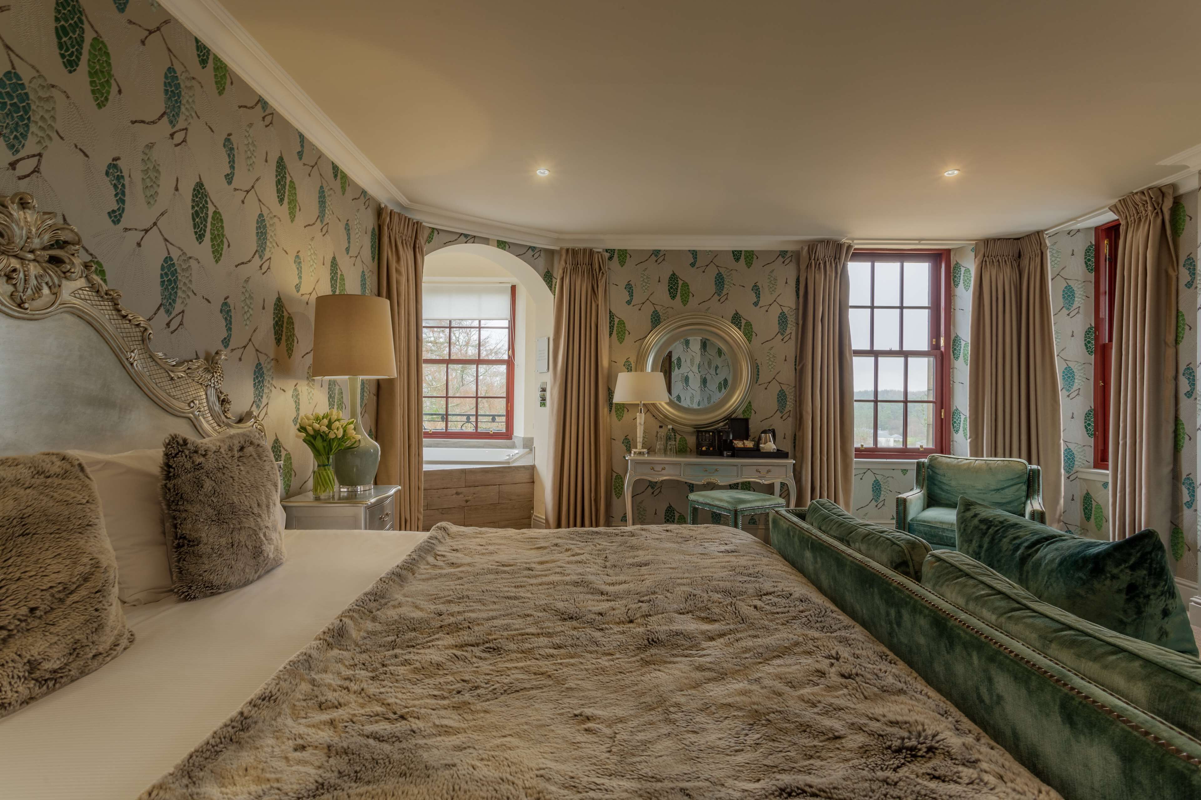 A bedroom with a large bed, a green sofa, a vanity with a mirror, and a window with curtains.