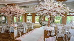 A wedding venue with white chairs, a white aisle, and large floral arrangements.
