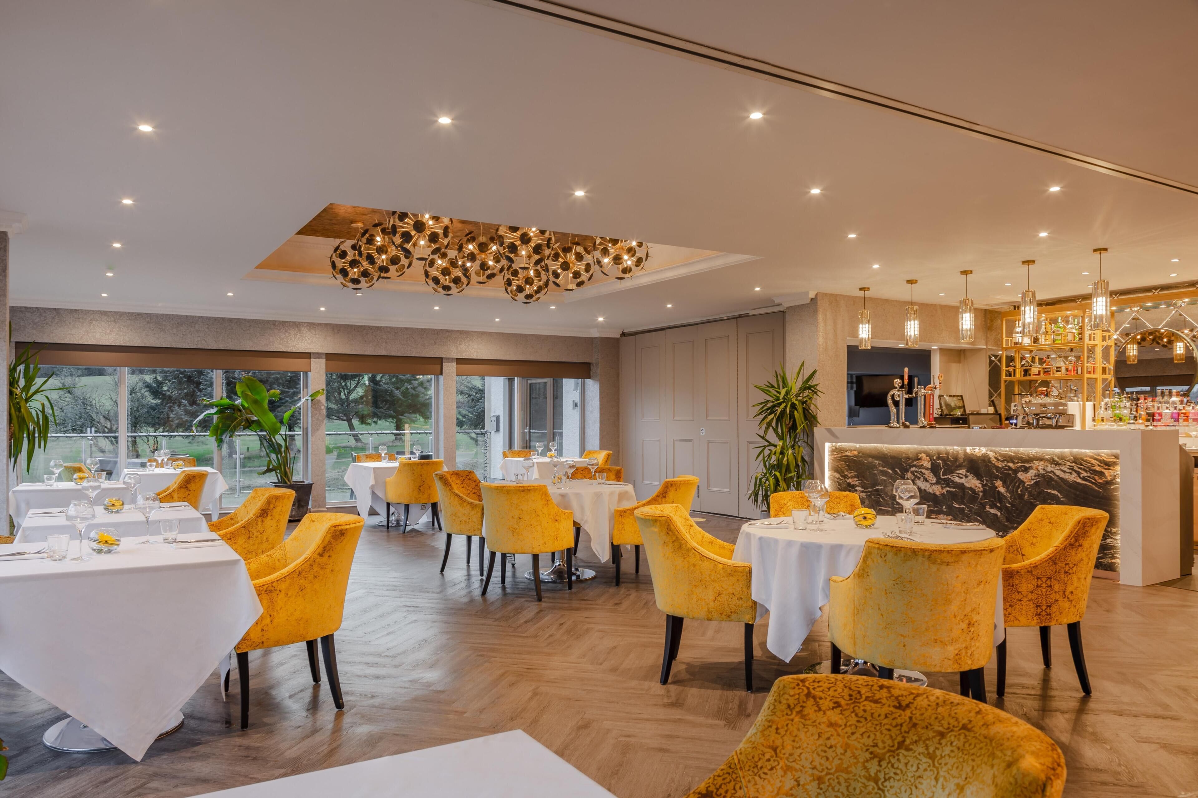 A restaurant with round tables, yellow chairs, and a bar area.