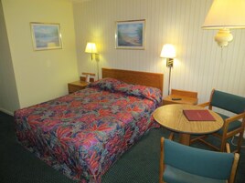 Habitación de hotel con cama, una mesa redonda de madera, dos sillas, una mesita de noche y dos lámparas fijadas a la pared.