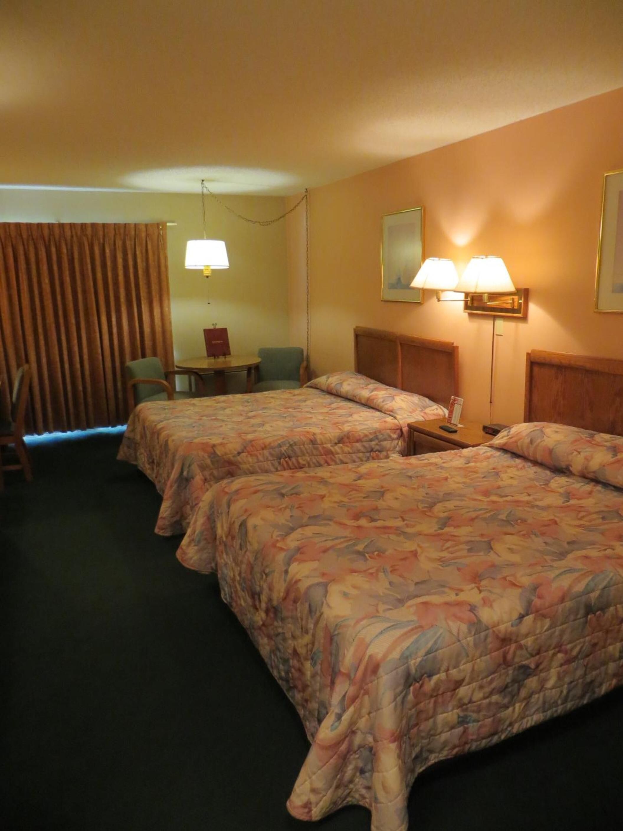 A hotel room with two beds, a desk, a chair, and a lamp.