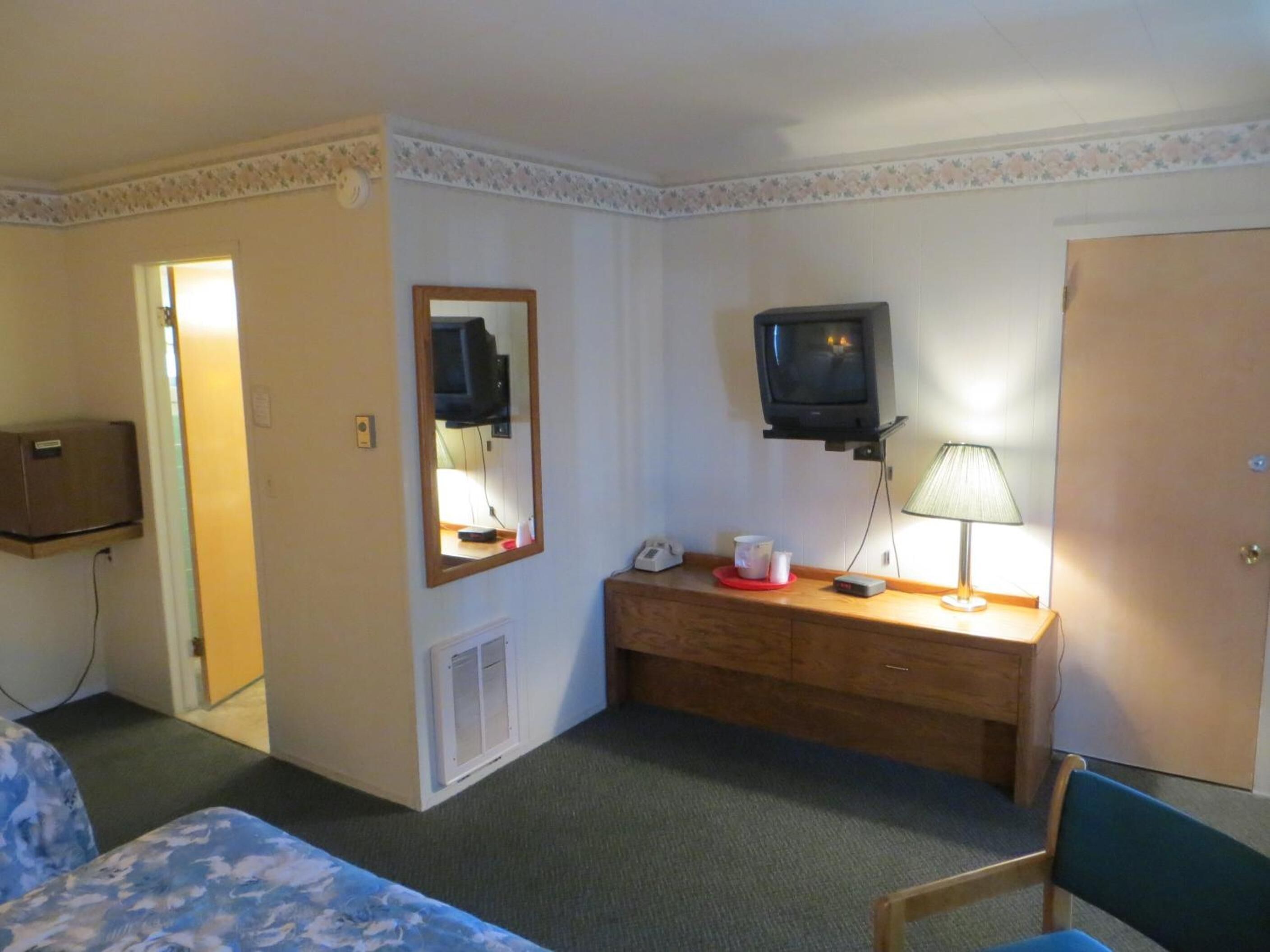 Een hotelkamer met een bed, een bureau met lamp, een televisie, een spiegel en een kledingkast.