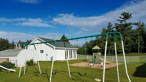A playground with swings and a slide, a small shed, and a building with a sign that reads "STANLEY". - Starlite Budget Inn (Mackinaw City)