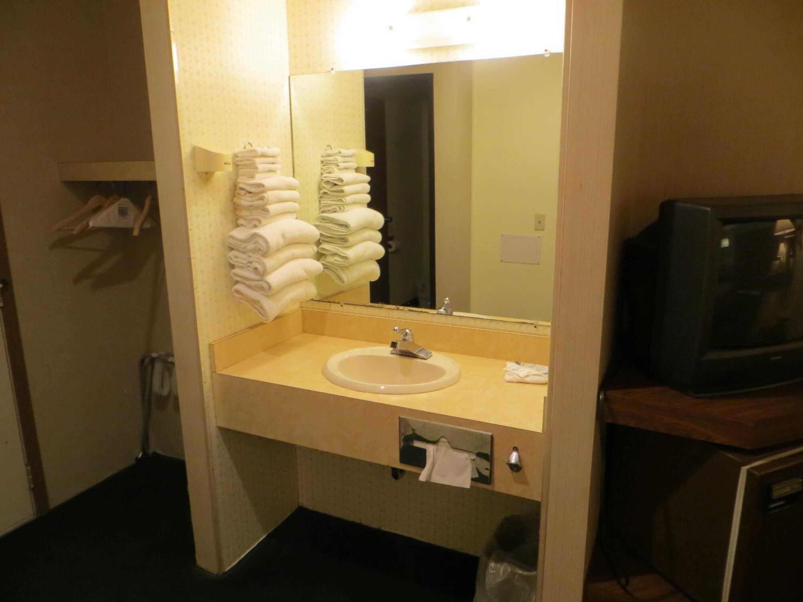 Ein Badezimmer in einem Hotel mit Waschbecken, Spiegel, Handtuchhalter und Fernseher.