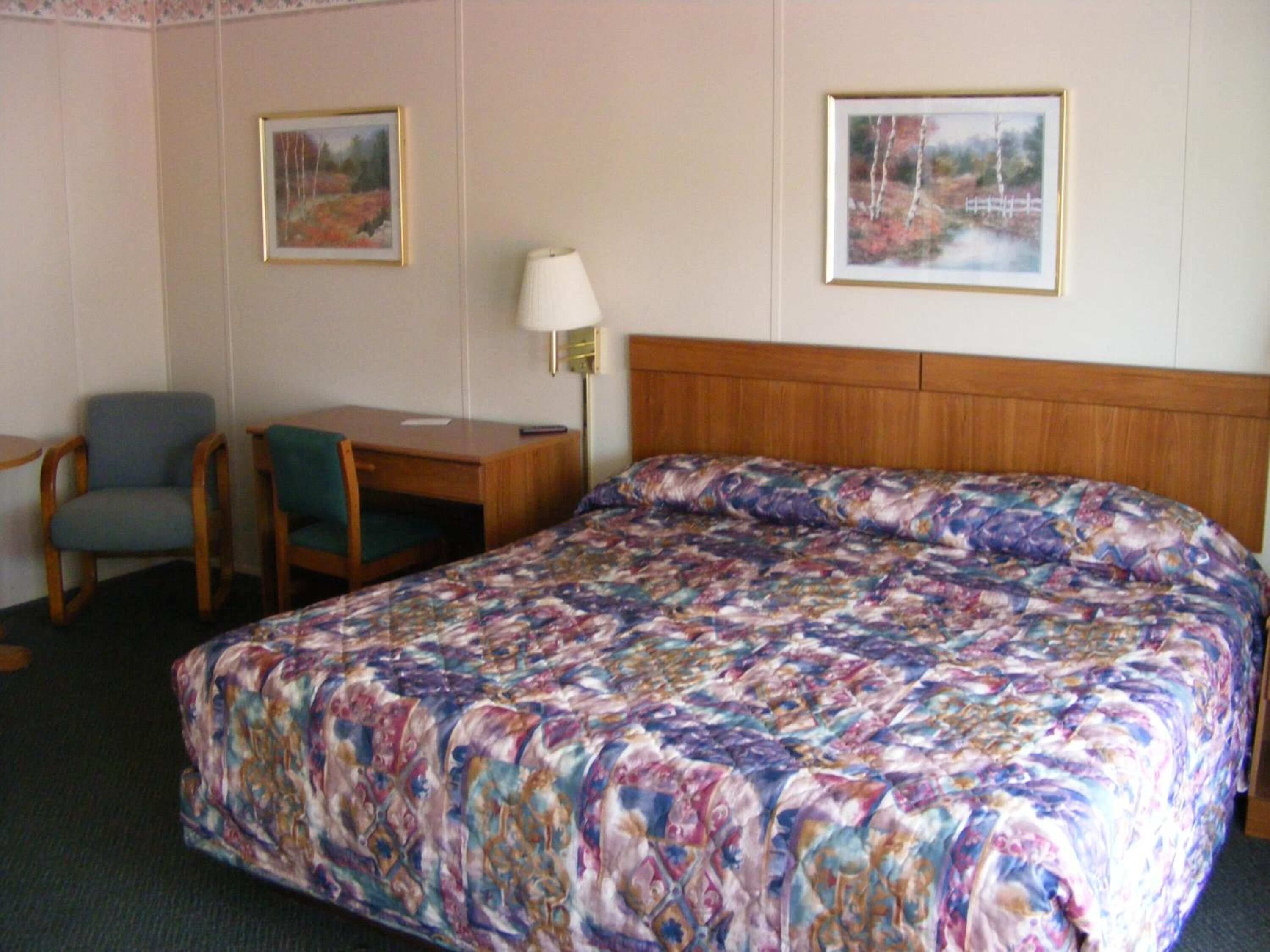 Habitación de hotel con una cama grande, un escritorio con dos sillas, una lámpara y dos cuadros en la pared.