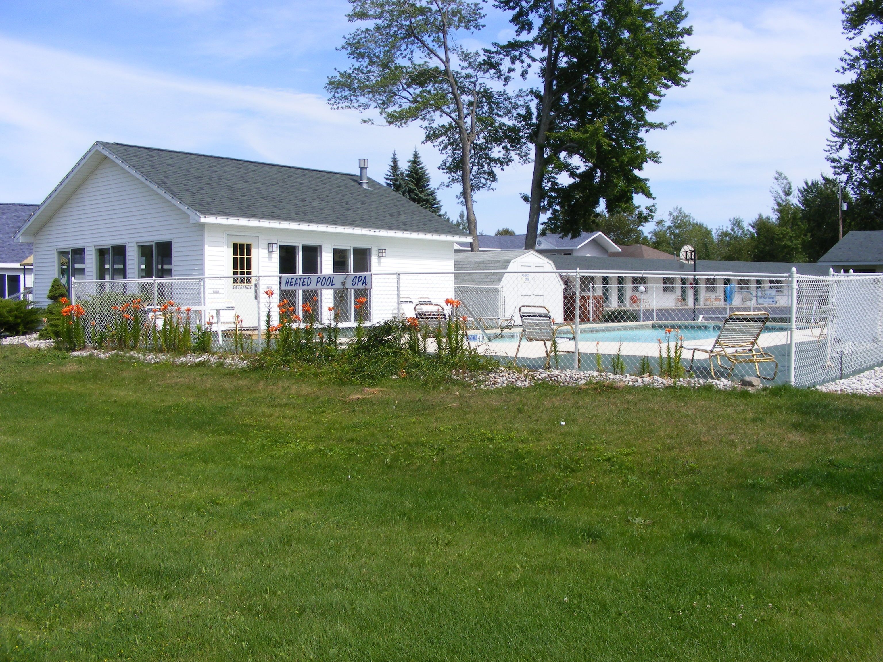 A white building with a sign reading "HEATED POOL SPA" and a fenced swimming pool area.