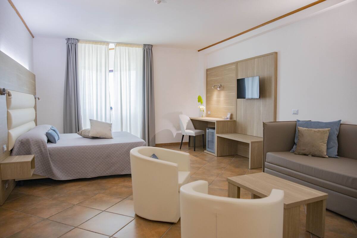 A modern hotel room with a bed, a desk, a sofa, and a TV.