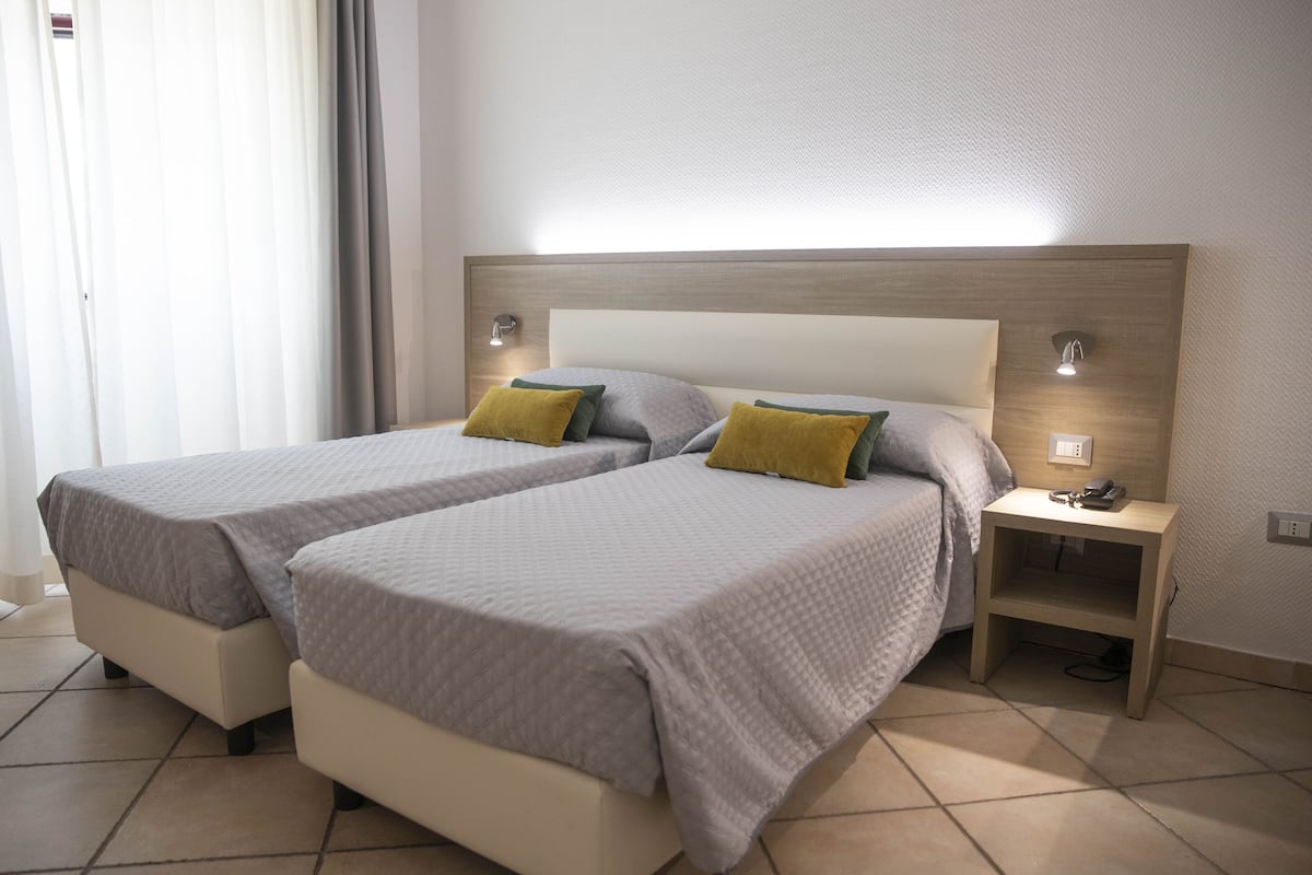 A hotel room with two beds, each with a headboard and bedside lamps.
