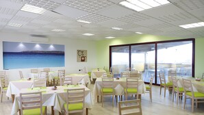 A dining area with tables and chairs, a large window with a view, and a painting on the wall. - Pegasus Hotel (Sassari)