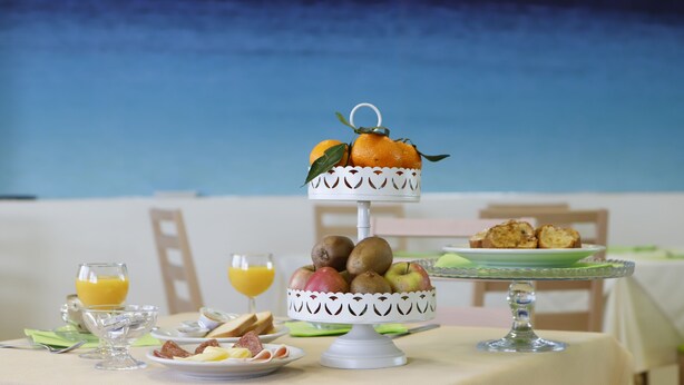 A breakfast table with a fruit display, plates of food, and glasses of orange juice. - Pegasus Hotel (Sassari)