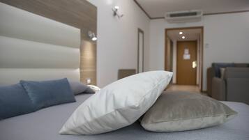 A modern hotel room with a large bed, two pillows, a wooden headboard, and a hallway leading to another room.