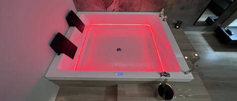 A modern spa with a heated floor, a large rectangular tub, and a decorative wall.