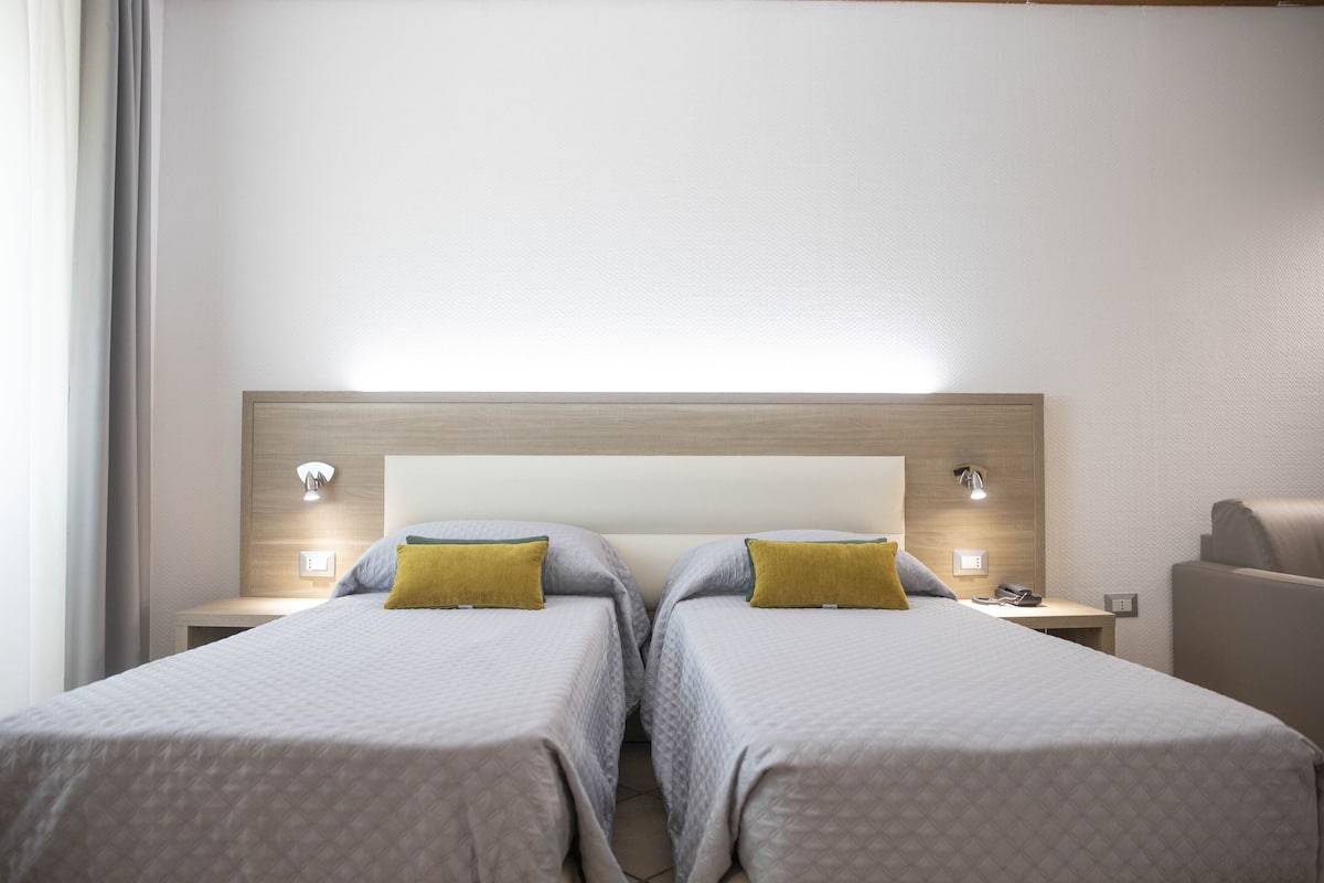 A hotel room with two beds, each with a pillow and a bedside table.