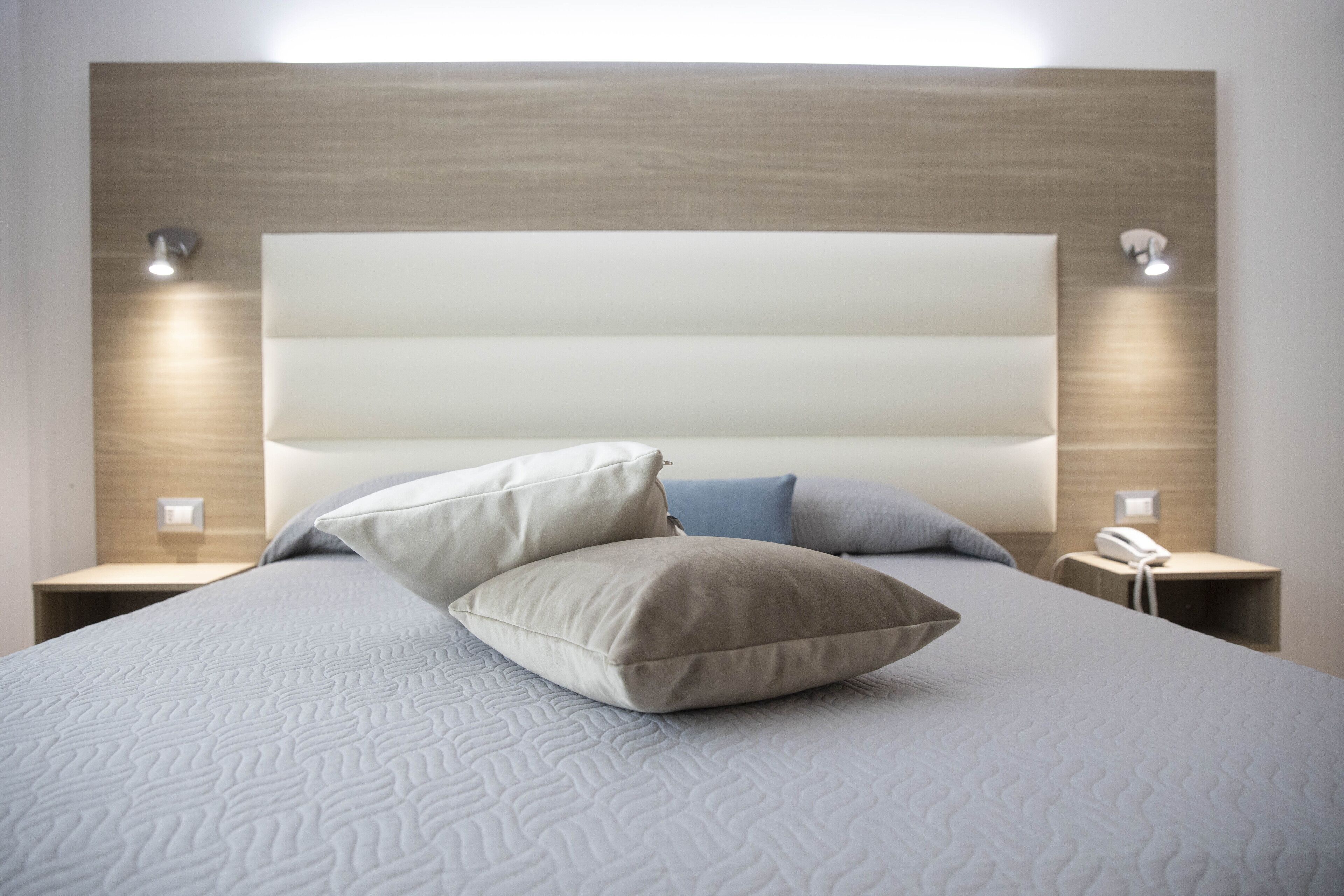 Una cama bien hecha con una colcha blanca texturizada y dos almohadas, un cabecero de madera y lámparas de noche.