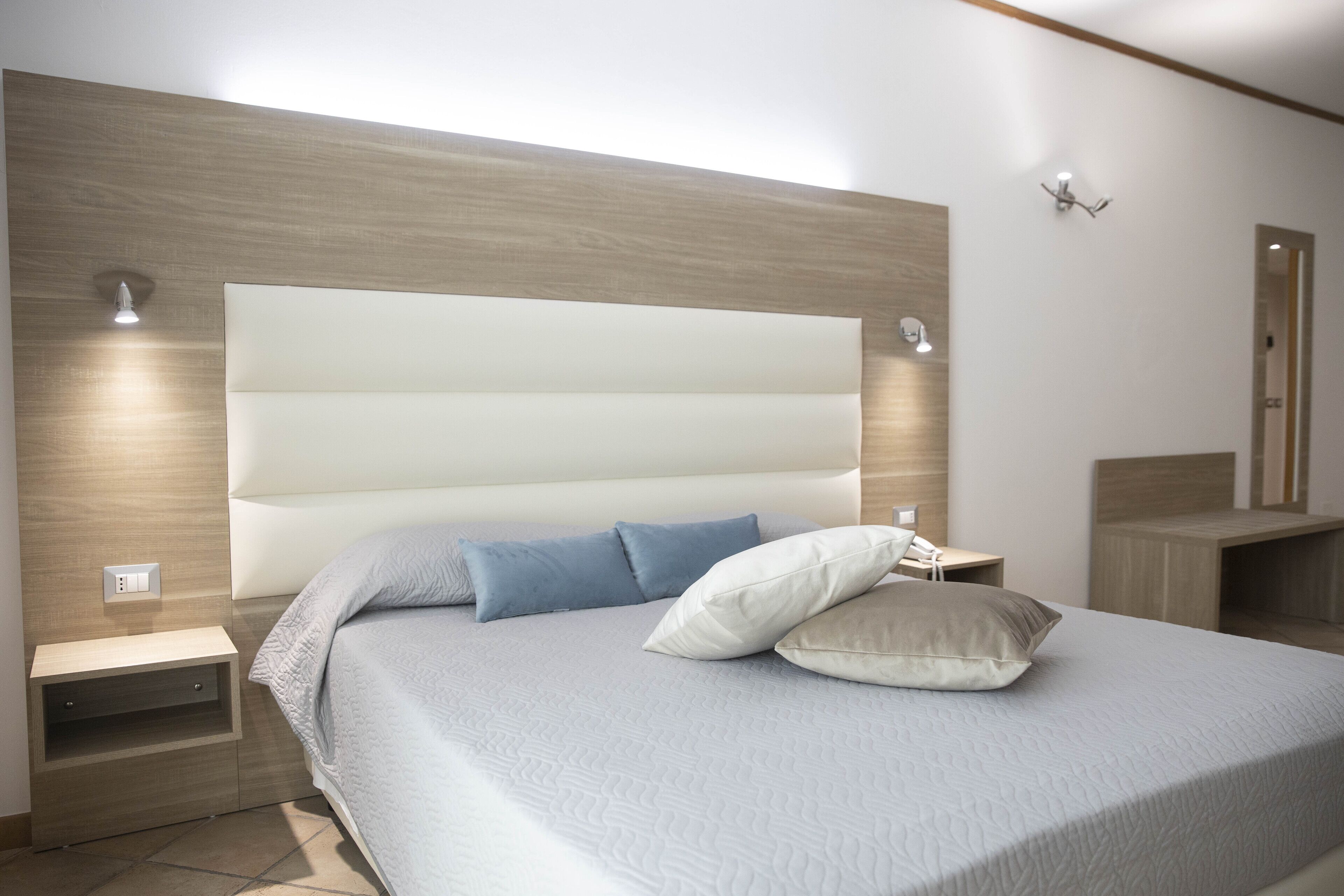 Une chambre moderne avec un grand lit, une tête de lit en bois, des tables de chevet et des lampes fixées au mur.