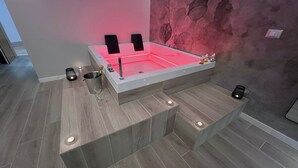 A modern bathroom with a heated floor, a large bathtub with red lighting, and two speakers. - Pegasus Hotel (Sassari)